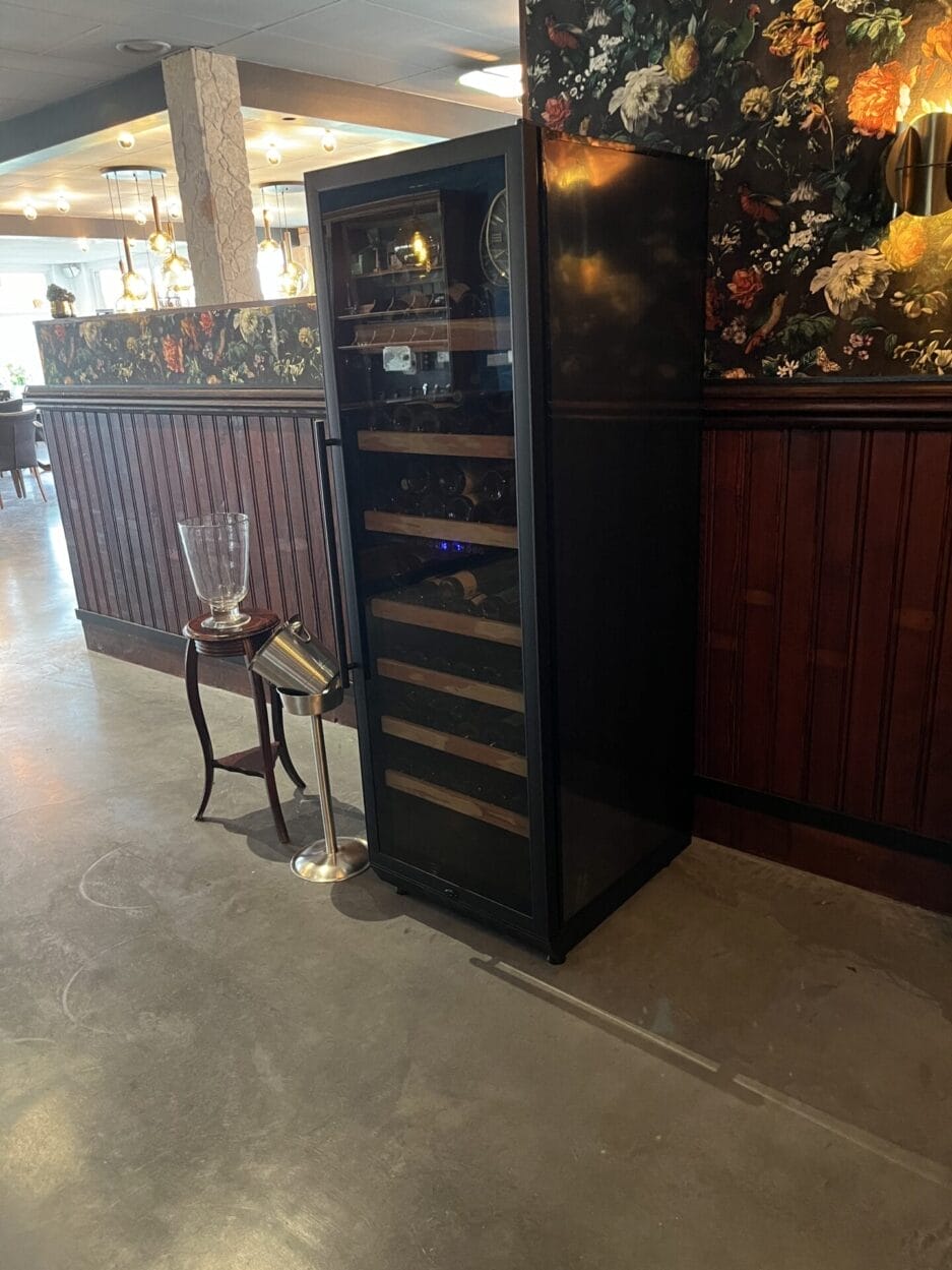 Wijnklimaatkast in een restaurant geplaatst tegen de achterwand, naast een bar.