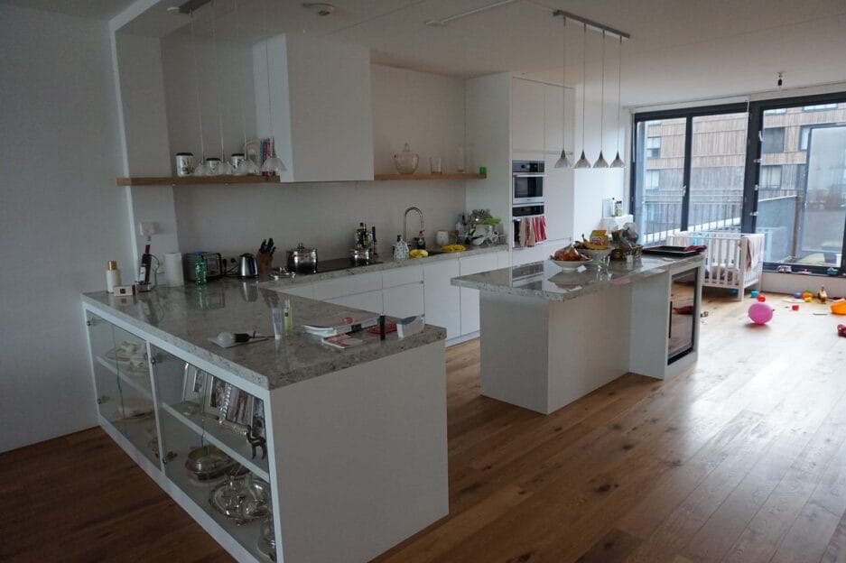 Moderne keuken met witte kasten en een centraal eiland, voorzien van een wijnbewaarkast voor het meteen uitserveren van de wijnen naar de eetkamer toe.
