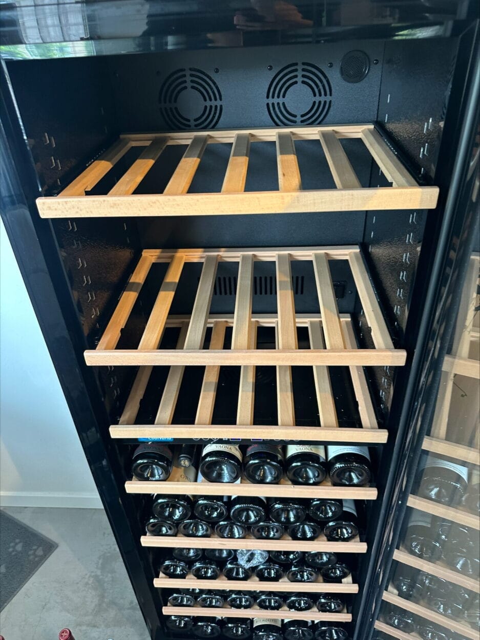 Een wijnklimaatkast met verschillende houten plateaus, sommige leeg en andere met flessen wijn, getoond vanaf de voorkant met de deur open.