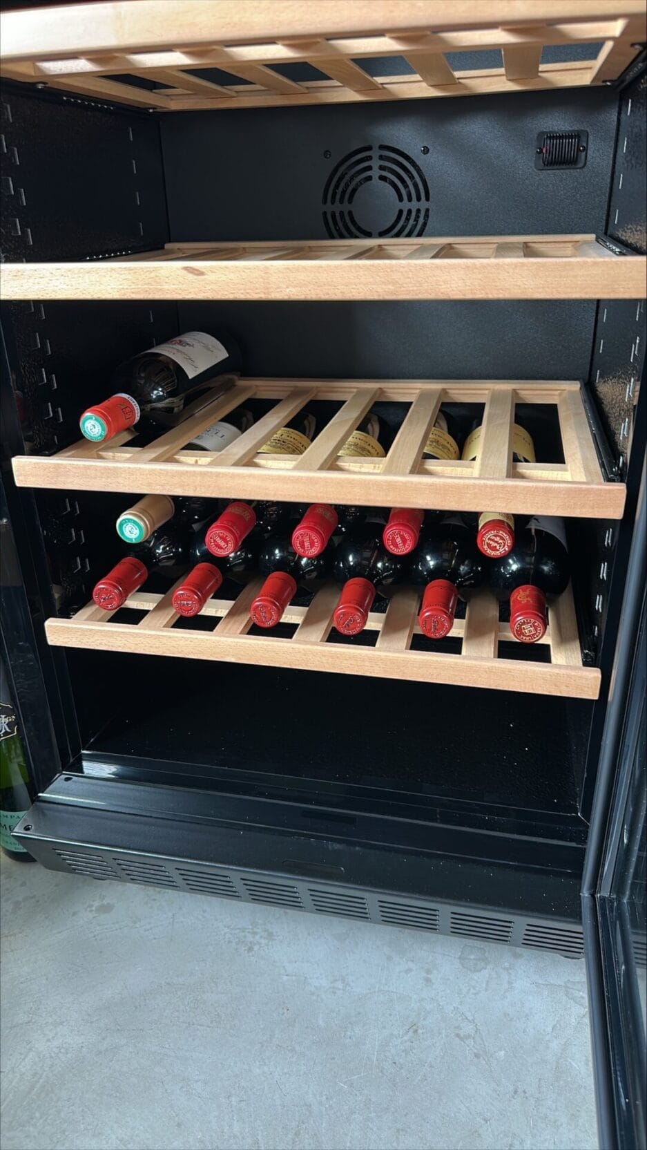 Een wijnkoelkast met houten planken bevat verschillende flessen wijn, de meeste met rode doppen, horizontaal gerangschikt.