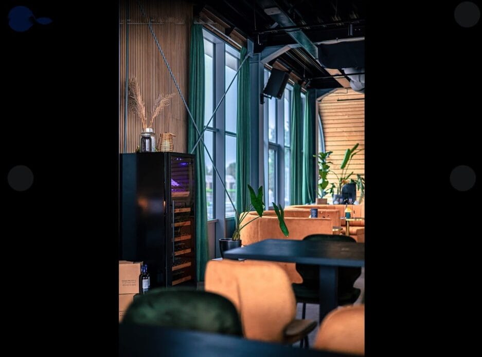 Een elegante lounge met zachte stoelen, een wijnkoeler en grote ramen met uitzicht op een stadsgezicht. de inrichting bestaat uit groene planten en warme verlichting.