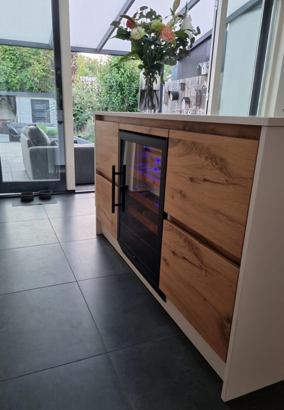 Een moderne houten keuken voorzien van een wijnbewaarkast waardoor deze zowel voor binnen als buiten direct bereikbaar is.