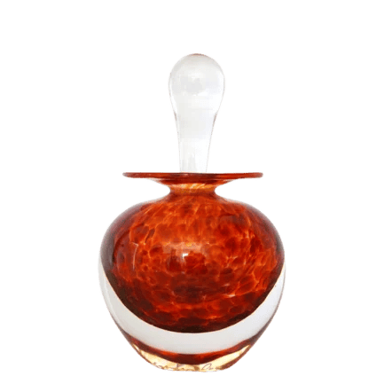 An orange, round glass perfume bottle with a transparent stopper, placed against a black background.