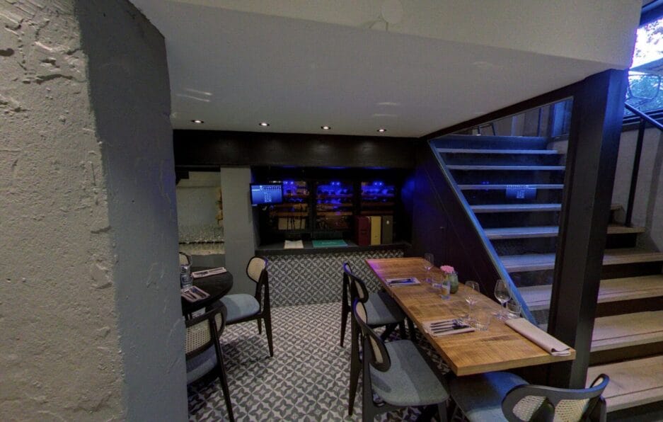 Interieur van een modern restaurant met in de kelder een bar, voorzien van wijn bewaarkasten, eettafels met stoelen.