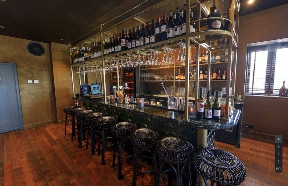 Interieur van een moderne bar met een selectie wijnen en sterke dranken, metalen barkrukken en een lange toonbank.
