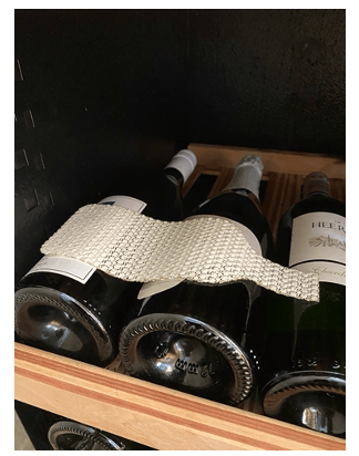 Wine bottles lie horizontally in a wooden rack, one covered with a textured silver fabric covering.