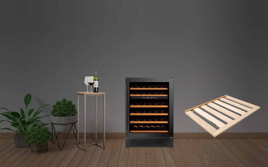 Une armoire à vin climatisée remplie de bouteilles se trouve à côté d'une petite table avec une bouteille de vin et des verres. Une planche de bois flotte à droite. Deux plantes en pot se trouvent à gauche.