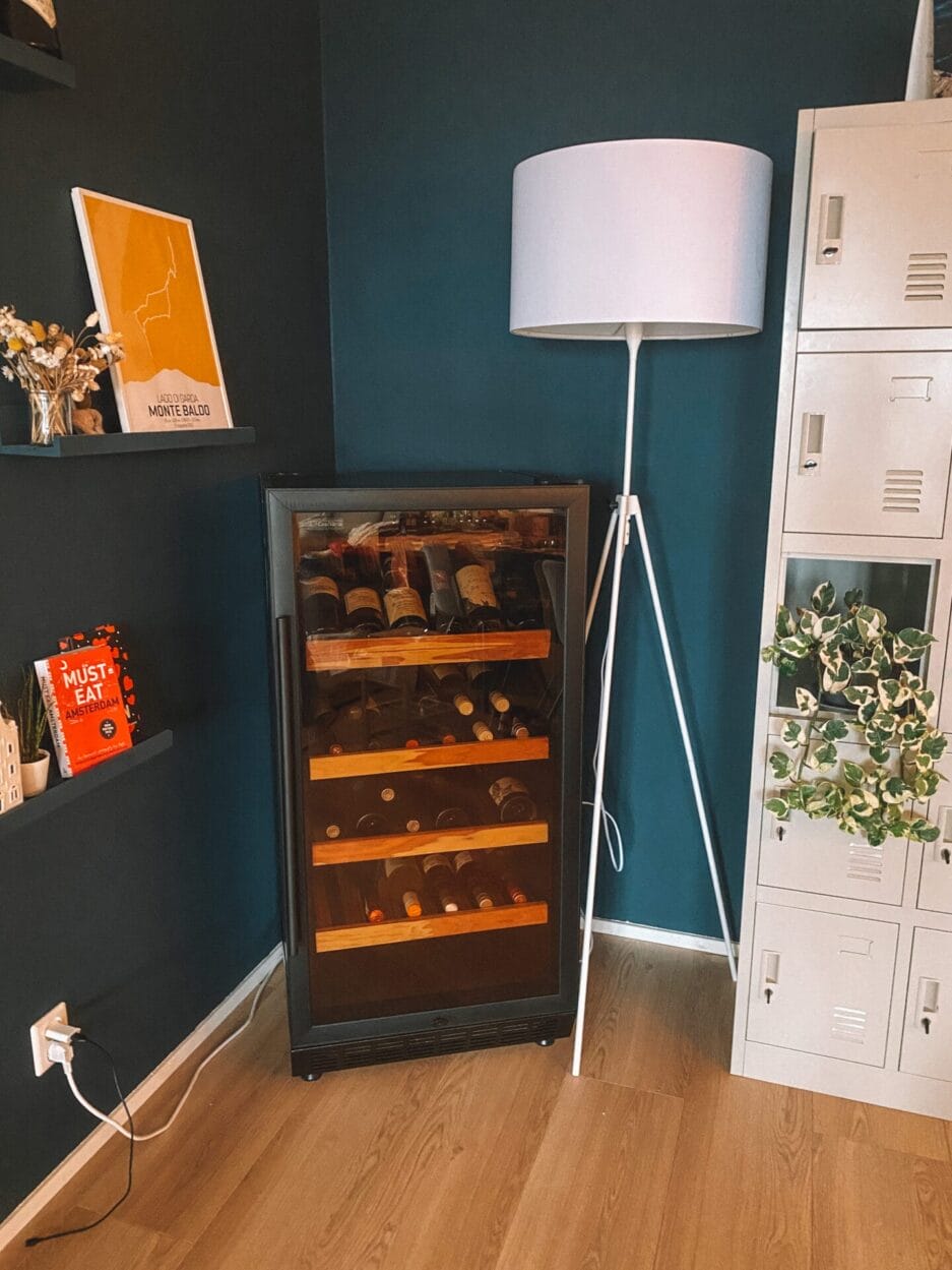Een wijnbewaarkast gevuld met flessen, naast een staande lamp, in een woonkamer.